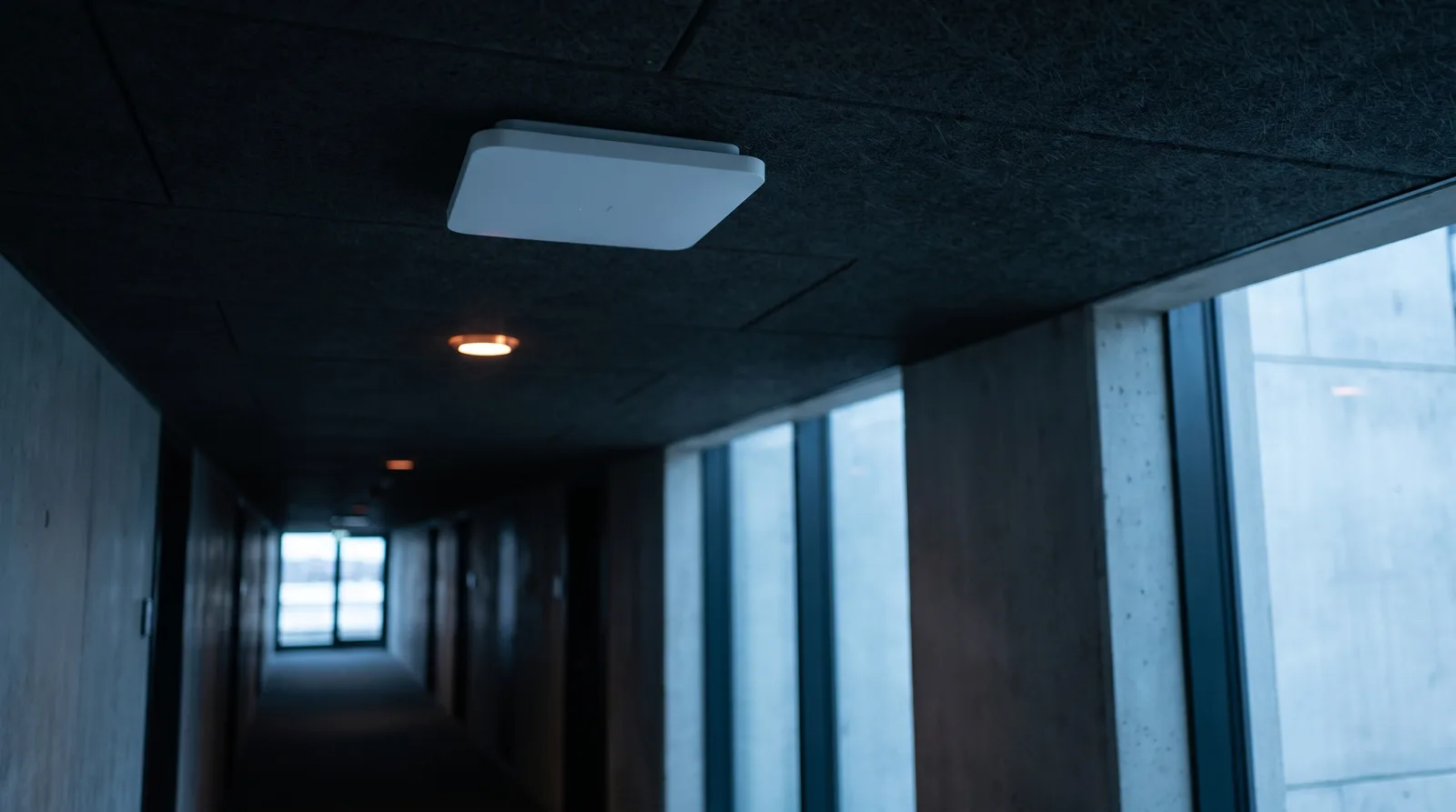 Punto de acceso en el cielo raso de un pasillo institucional, el corredor perdiéndose en penumbra