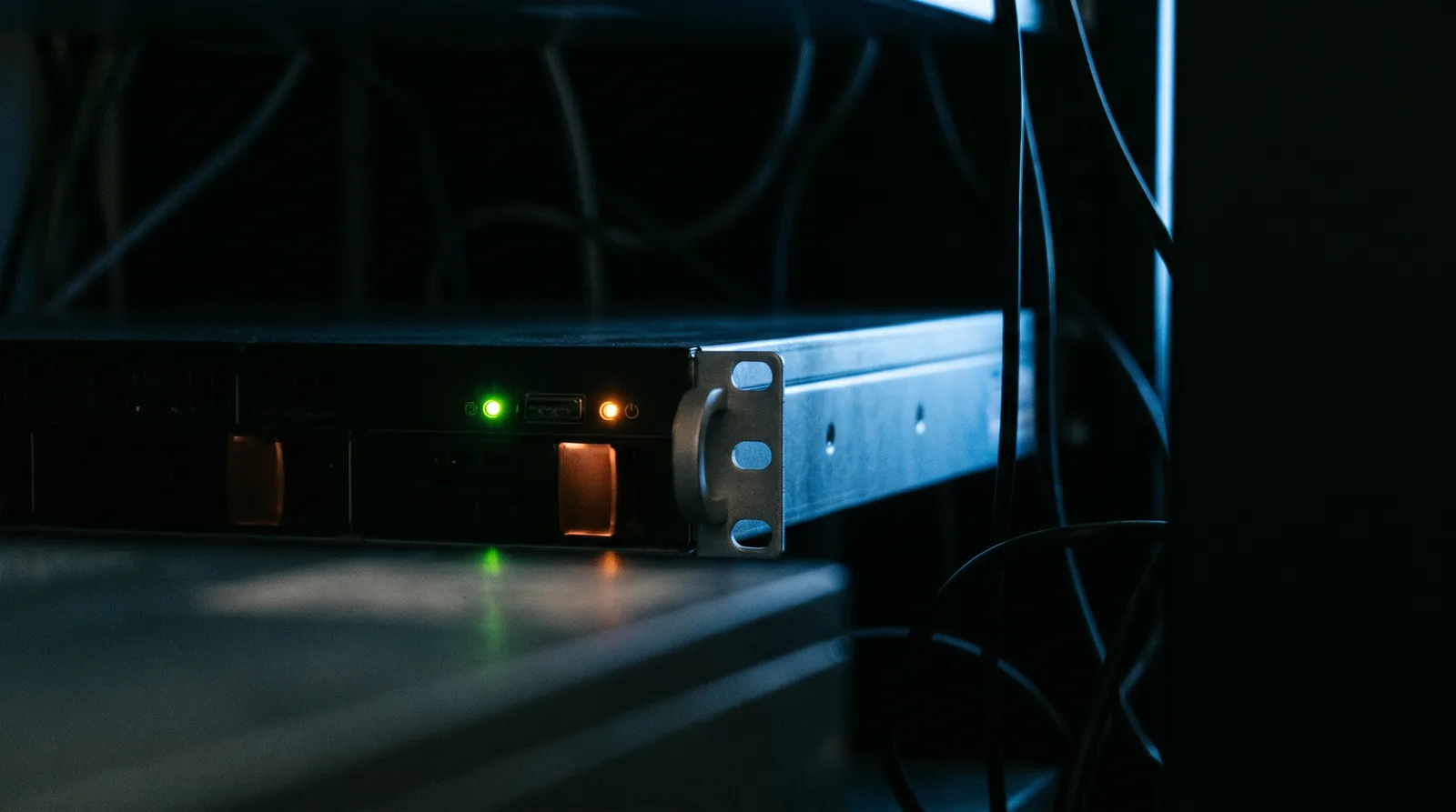 Un solo servidor encendido en un cuarto de equipos a oscuras, sus indicadores como única luz
