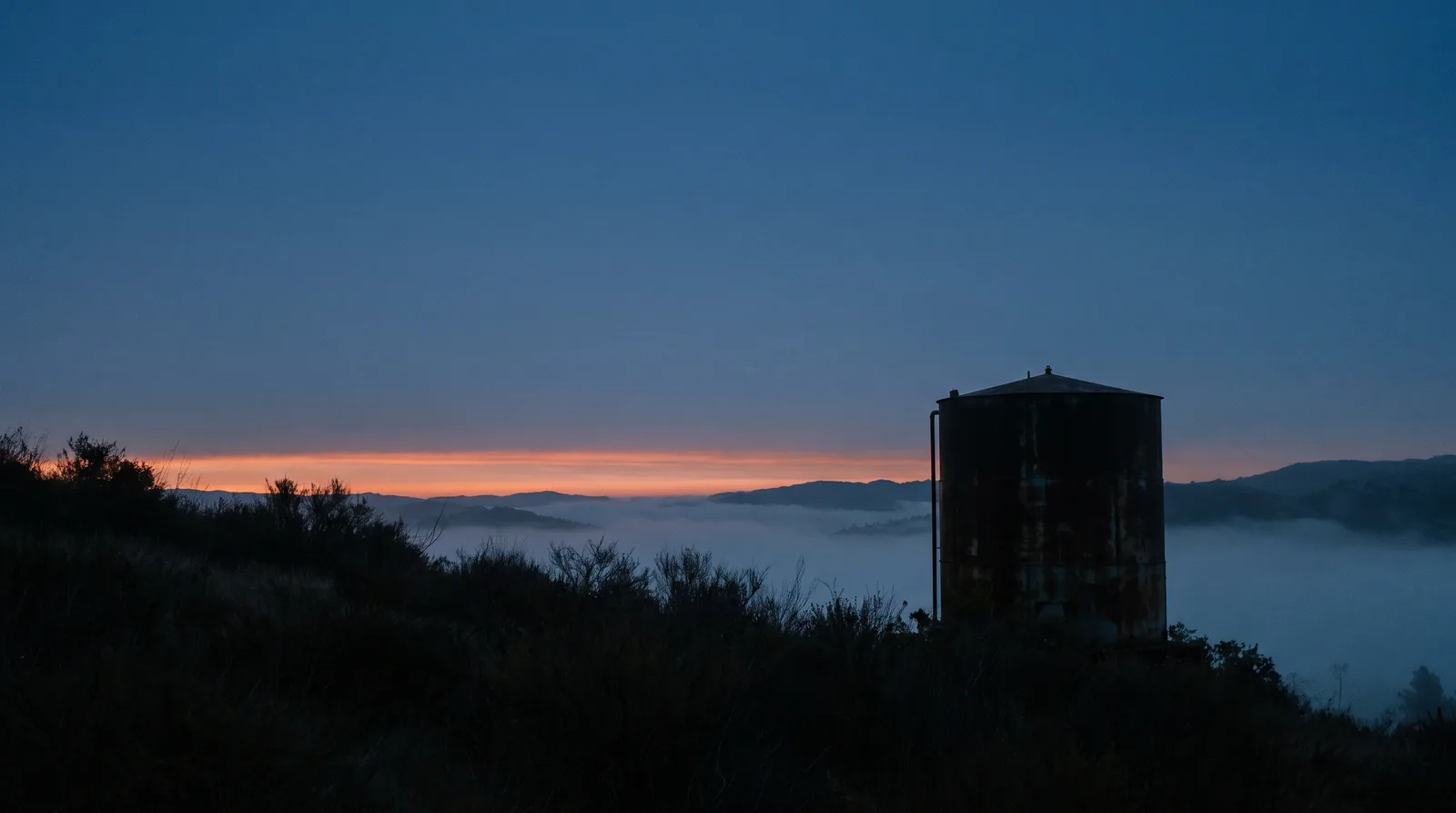 Tanque de un acueducto rural en una ladera al amanecer, con neblina en el valle
